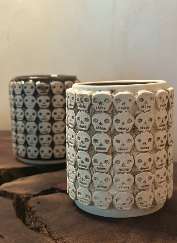 Vaso blanco y vaso negro de cerámica con diseño de calaveras inspiradas en los tzompantlis.